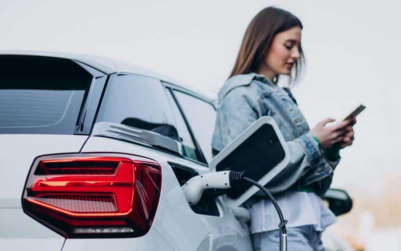 female charging electric vehicle while on phone with mobile software app